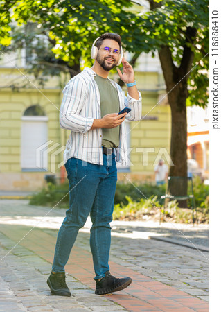 Happy young man putting on headphones listening favorite energetic music in smartphone on street 118888410