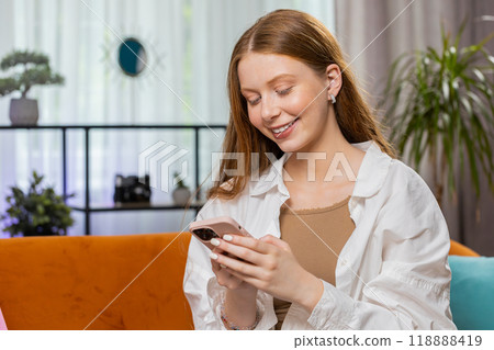 Girl sitting on sofa using smartphone share messages on social media application watching movies Girl sitting on sofa using smartphone share messages on social media application watching movies 118888419