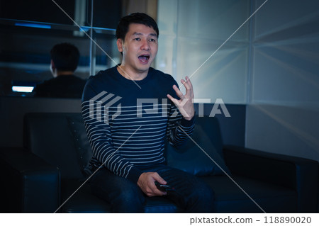 shocked and scared man is watching horror movie TV on sofa at night 118890020