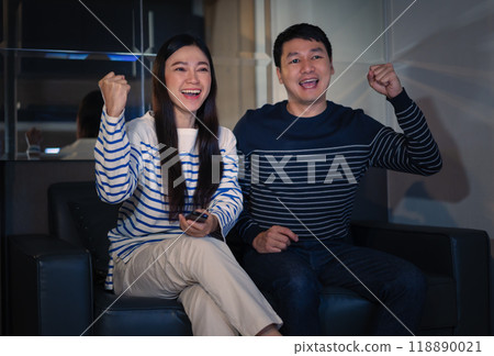 cheerful couple watching sport TV with arm raised on sofa at night 118890021