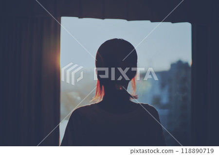 Silhouette of a woman watching the sunset through a window 118890719