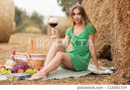 Woman in dress sitting with wine during picnic Woman in dress sitting with wine during picnic 118891334