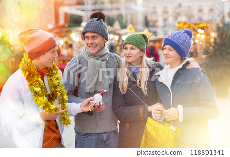 Portrait of man and woman and their happy teenagers posing with paper bags near counters at Christmas fair Portrait of man and woman and their happy teenagers posing with paper bags near counters at Christmas fair 118891341