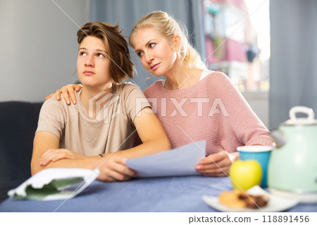 Worried woman with upset teenage son reading paper letter with bad news Worried woman with upset teenage son reading paper letter with bad news 118891456