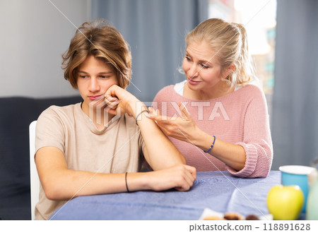 Caring mother soothing upset teenage boy at home table 118891628