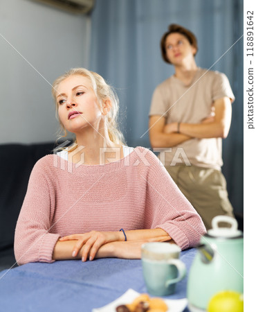 Upset woman sitting at home after disagreements with teenage son 118891642