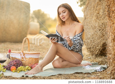Beautiful young woman in checkered shirt resting near haystack in middle of wheat field on summer evening 118891688