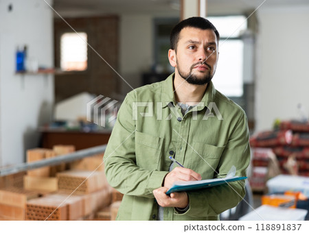 Engineer planning renovation works at building site, looking at papers 118891837