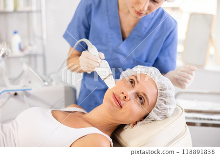 Young female patient undergoing facial skin cleansing with ultrasonic shovel 118891838