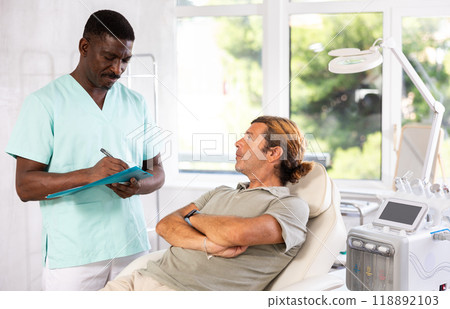 African American cosmetologist filling out medical form for male patient African American cosmetologist filling out medical form for male patient 118892103