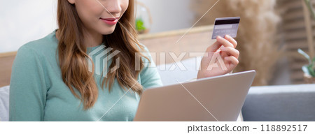 Young asian woman sitting on sofa using laptop computer shopping online with credit card. 118892517