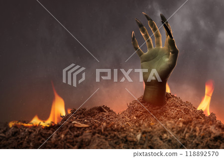 Witch hand with long black nail coming out from grave ground with a fire in the background. The hand appearing to be a evil, satan, zombie or a monster hand 118892570