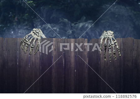 Human skeleton hand rising out of behind wooden fence, with a creepy, dark and scary mood. The skeleton hand appearing to be a devil, evil, satan, zombie or a monster hand Human skeleton hand rising out of behind wooden fence, with a creepy, dark and scary mood. The skeleton hand appearing to be a devil, evil, satan, zombie or a monster hand 118892576