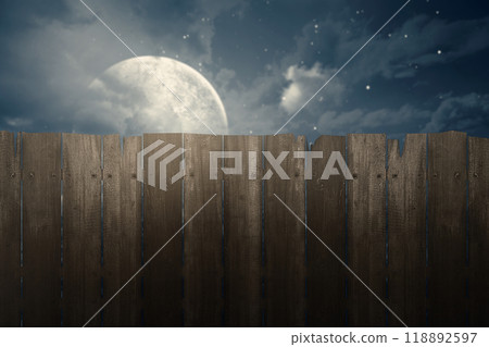 A wooden fence with a moon in the sky behind it. The moon is large and bright, casting a shadow on the fence 118892597