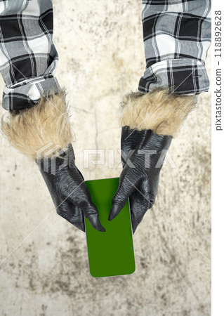 Werewolf hand with fur and black claws holding a mobile phone or cell phone. Blank mobile phone screen for copy space. Scary werewolf, wolfman, or animal monster 118892628