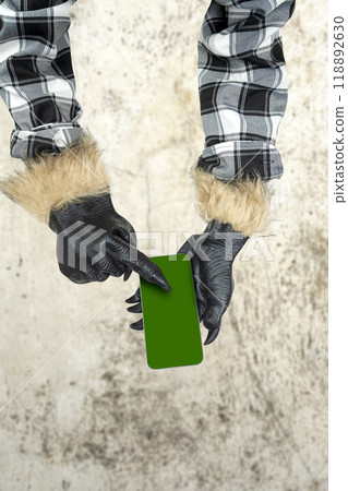 Werewolf hand with fur and black claws using a mobile phone or cell phone. Blank mobile phone screen for copy space. Scary werewolf, wolfman, or animal monster 118892630