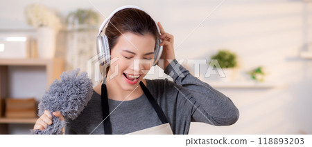 Young asian woman dusting while listening to music with headphones in a bright. 118893203