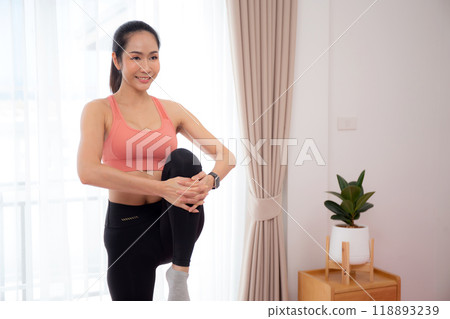 Beautiful young asian woman standing workout with warmup and stretch muscle leg at home. 118893239