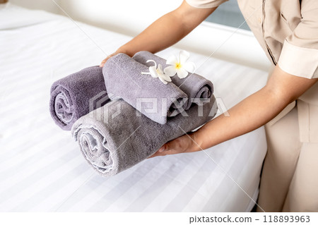 Hands of hotel maid putting plumeria flower and towels on the bed in the luxury hotel room ready for tourist travel Hands of hotel maid putting plumeria flower and towels on the bed in the luxury hotel room ready for tourist travel 118893963