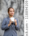 Young happy Asian businesswoman in a suit holding a mug of coffee, standing confident against the black and white background 118894109