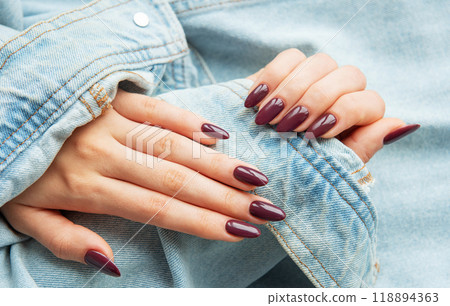 Elegant hands with polished burgundy nails resting on a denim jacket sleeve Elegant hands with polished burgundy nails resting on a denim jacket sleeve 118894363