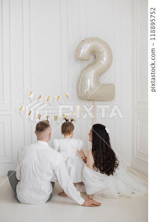 Family celebrating toddler's second birthday with balloon and decorations 118895752