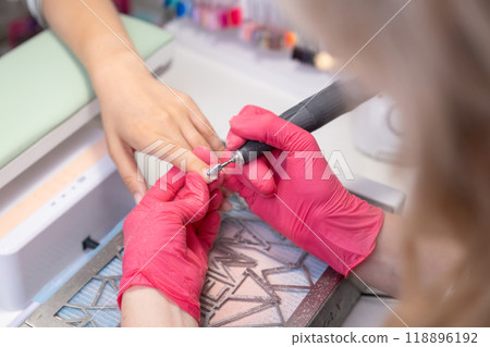 Manicure master uses a drill machine for nail polish removing in beauty salon. 118896192