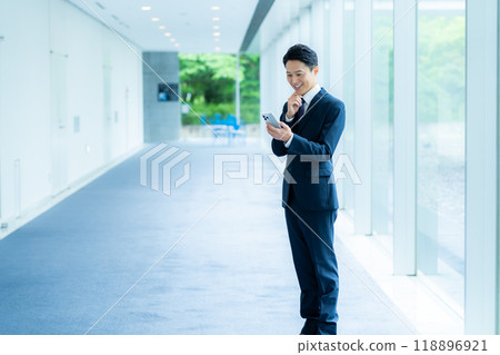 A businessman operating a smartphone in an office corridor A businessman operating a smartphone in an office corridor 118896921