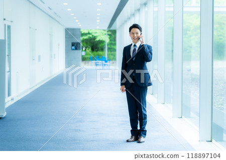 A businessman operating a smartphone in an office corridor A businessman operating a smartphone in an office corridor 118897104