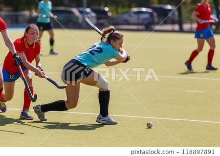 Female attacker hitting the ball in an intense field hockey match on a sunny afternoon 118897891
