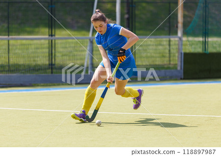 Young female player running with the ball in a field hockey match Young female player running with the ball in a field hockey match 118897987