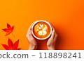 Top View Female Hands Hold Cup with Pumpkin Coffee, Spice Latte, Cappuccino. Hot Drink, Beverage in Autumn. Red Leaves on Yellow Background. Copy Space 118898241