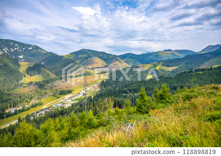 A panoramic view captures the beauty of the Jasna Mountain Resort nestled under Chopok Mountain in the Low Tatras. Lush greenery and mountain slopes create a picturesque landscape on a bright day. A panoramic view captures the beauty of the Jasna Mountain Resort nestled under Chopok Mountain in the Low Tatras. Lush greenery and mountain slopes create a picturesque landscape on a bright day. 118898819