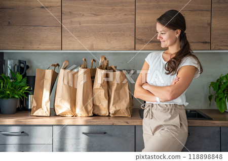 Young woman next to paper bags full of food in kitchen. Groceries ordered online and delivered by courier 118898848
