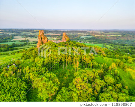 The Trosky castle ruins rise above the lush green landscape of Bohemian Paradise, offering a stunning aerial view in the early morning light, surrounded by dense trees and rolling hills. 118898867