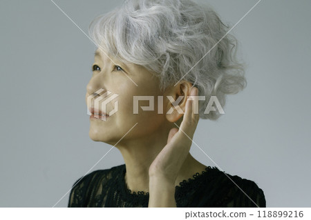 A gray-haired senior woman holding her hand over her ear 118899216