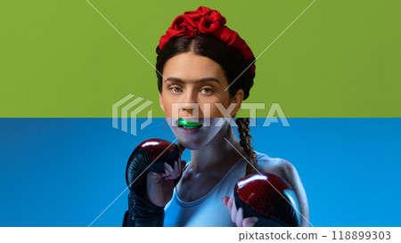 Frida boxer. Creative collage. Woman styled like Frida Kahlo with red headpiece, in boxing gloves, biting green mouth guard. Frida boxer. Creative collage. Woman styled like Frida Kahlo with red headpiece, in boxing gloves, biting green mouth guard. 118899303