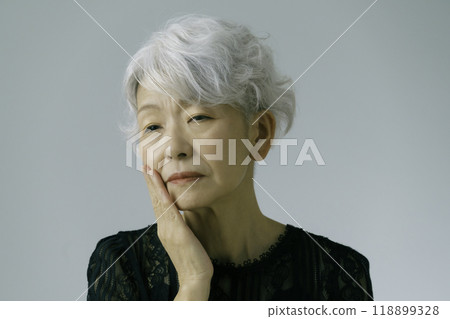 A gray-haired senior woman with her hand on her cheek 118899328