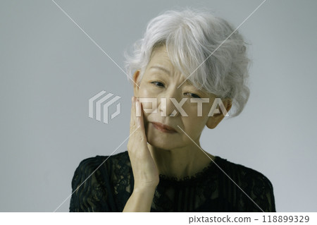A gray-haired senior woman with her hand on her cheek 118899329