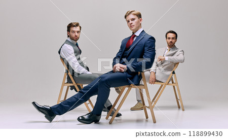Group of young men sitting on chairs in relaxed pose. They exude confidence and composure while maintaining professional demeanor. Group of young men sitting on chairs in relaxed pose. They exude confidence and composure while maintaining professional demeanor. 118899430