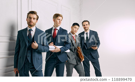 The team poses confidently against white studio background, each holding work-related materials, ready for their next business venture. The team poses confidently against white studio background, each holding work-related materials, ready for their next business venture. 118899470