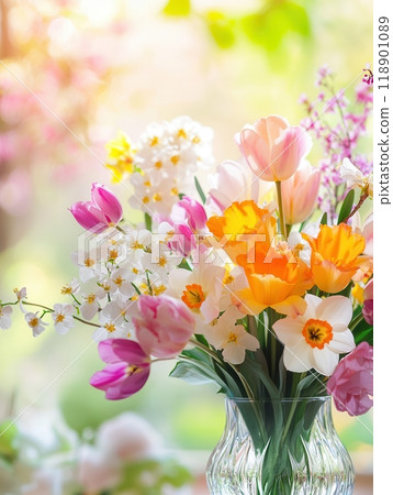 A colorful bouquet of tulips, daffodils, and cherry blossoms is beautifully arranged in a glass vase, brightening the room. 118901089