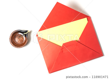 Happy Diwali greetings: Vibrant red envelope with blank note for festive greetings beside it traditional burning clay oil lamp on white background. 118901471
