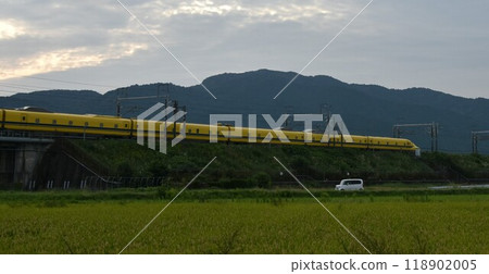 A yellow Shinkansen train racing through the Showa era countryside 118902005