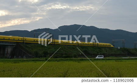 A yellow Shinkansen train racing through the Showa era countryside 118902006