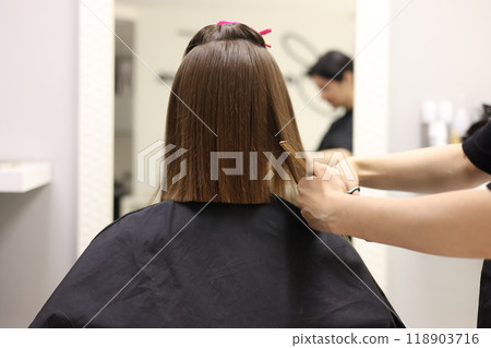 Unrecognisable hairdresser cutting female client hair with professional barber scissors and comb and making stylish haircut short bob hairstyle in beauty salon. Hair care, hair salon and hairstyling 118903716