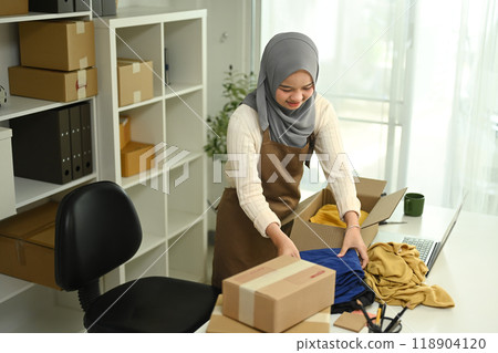 Young Muslim female entrepreneur packing parcels for delivery. E-commerce concept 118904120