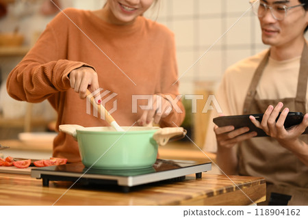 Young couple cooking together in their kitchen and following a recipe on digital tablet Young couple cooking together in their kitchen and following a recipe on digital tablet 118904162