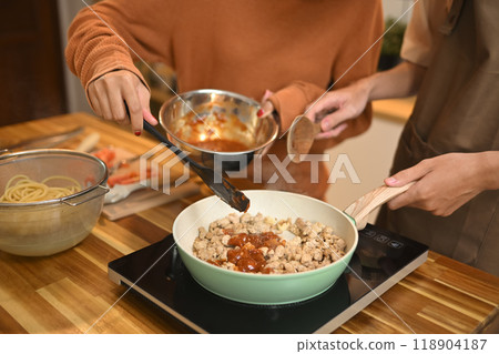 Close up shot of young couple cooking, stirring ingredients in frying pan with wooden spatula 118904187