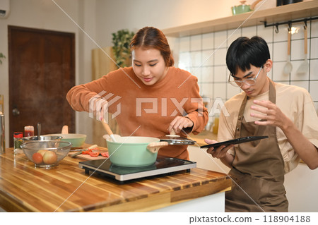 Young couple cooking together in their kitchen and following a recipe on digital tablet 118904188